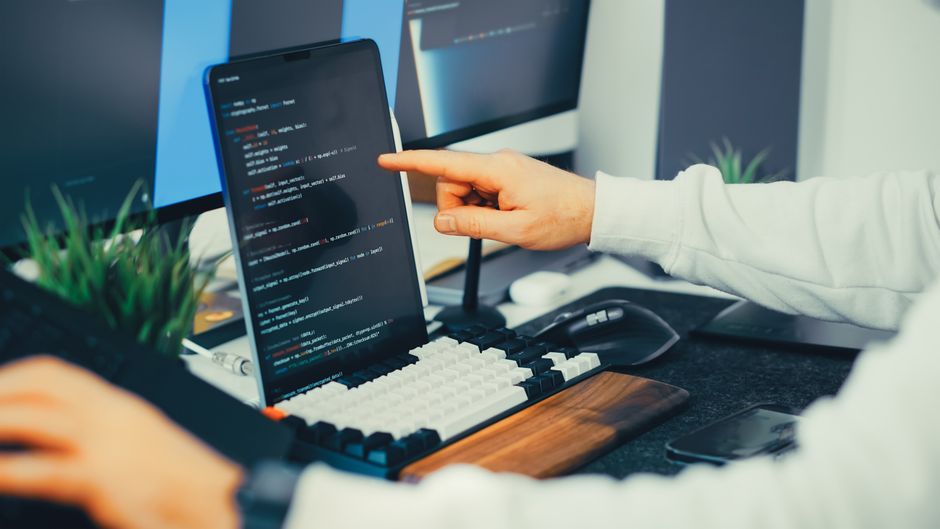 A programmer working on code with a laptop and monitor setup in an office. — illustrating cline vscode